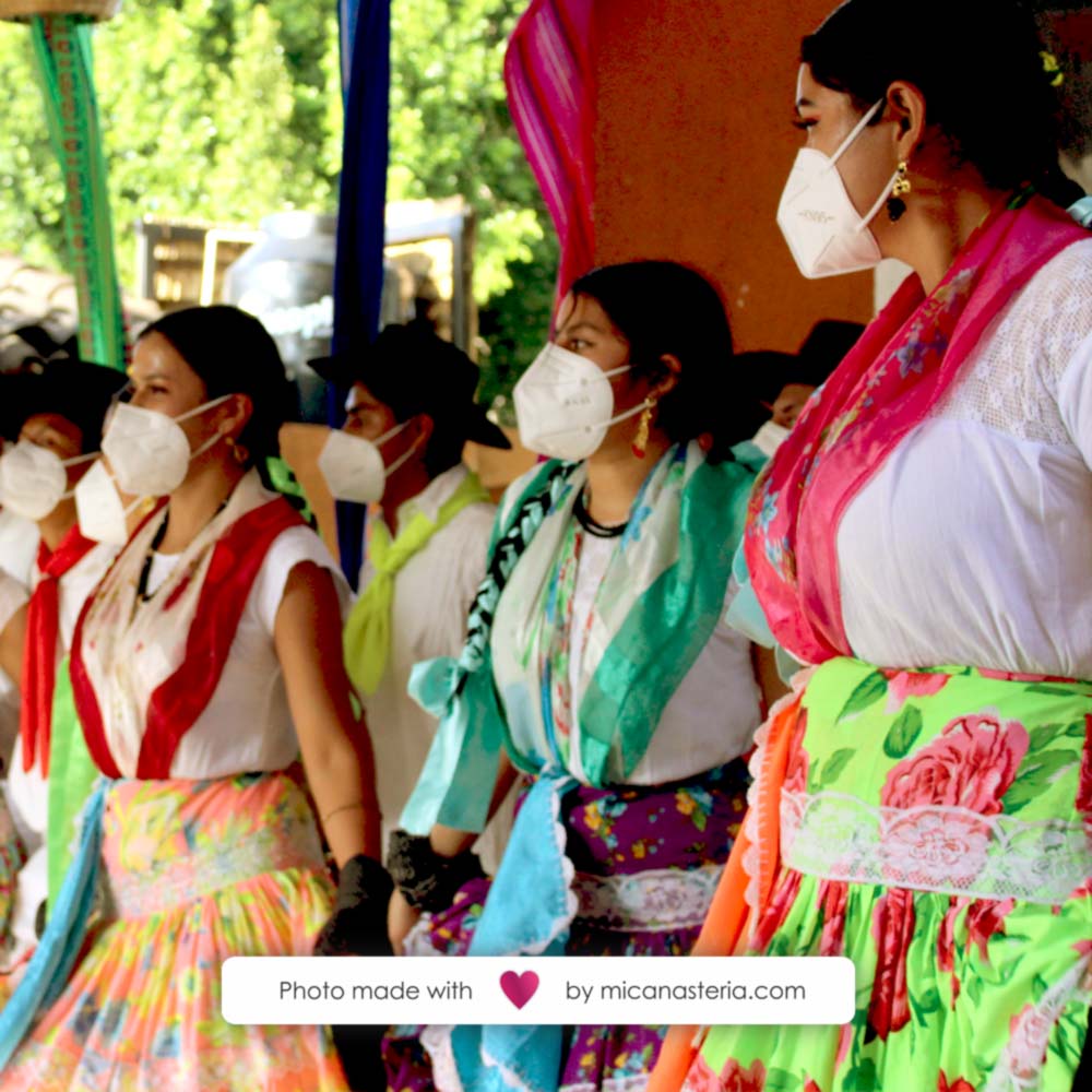 Mujeres bailando con trajes típicos de la región y usando cubrebocas.